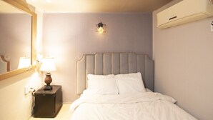 A hotel room with a bed, a nightstand with a lamp, a wall-mounted light fixture, and an air conditioning unit. - Maison Yongsan Hotel (Seoul)