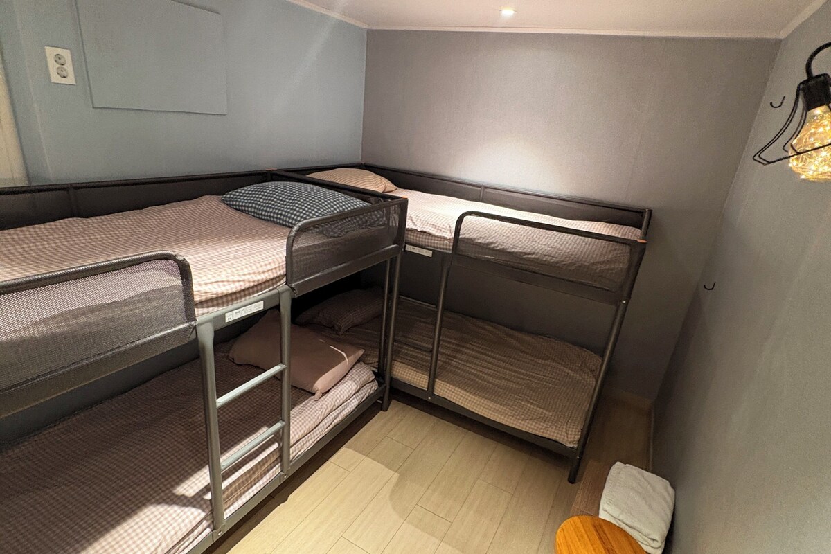 A compact room with bunk beds, a small wooden stool, and a light fixture on the wall.