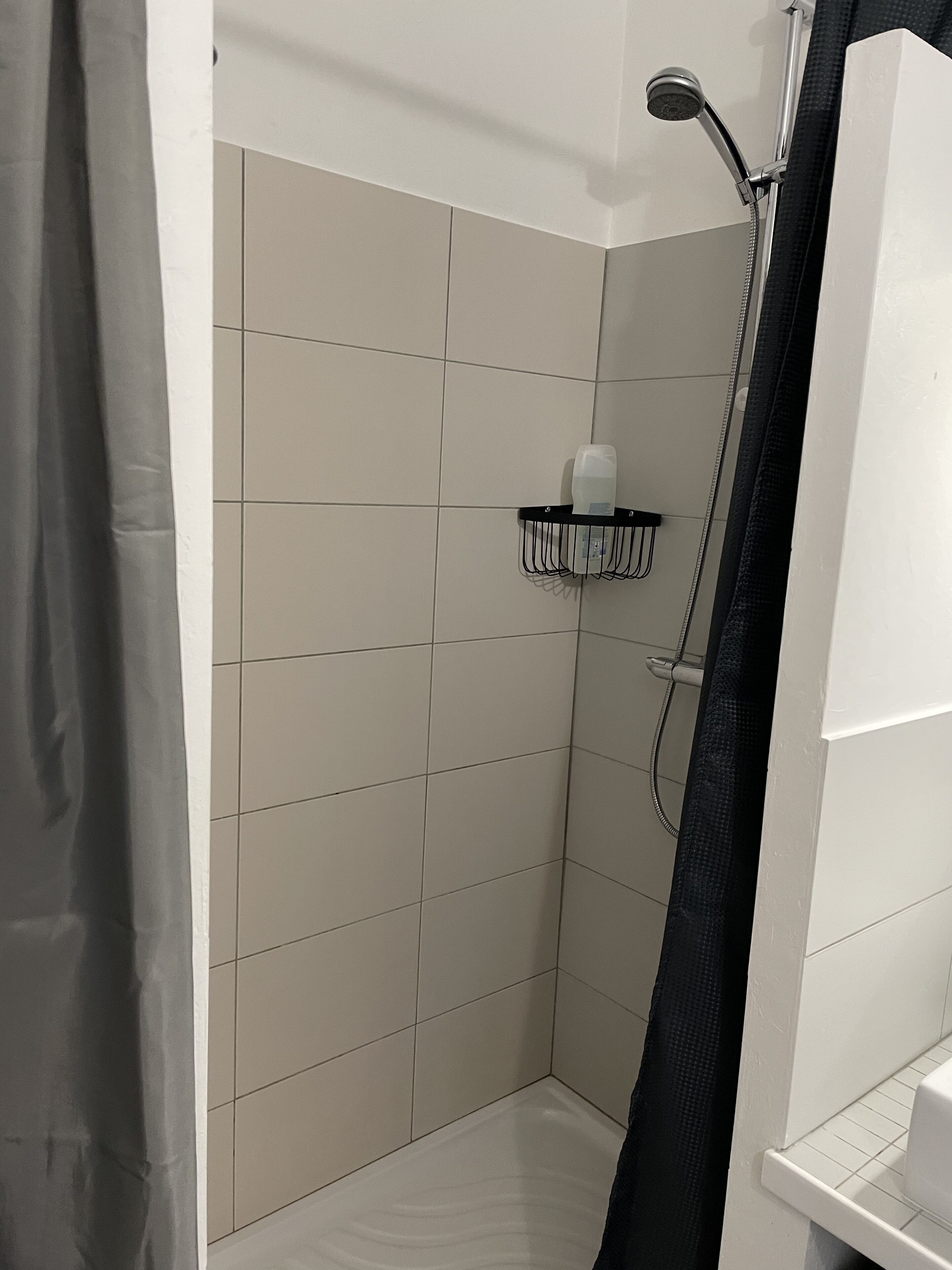 A small, tiled shower area with a showerhead, a soap dispenser, and a towel rack.