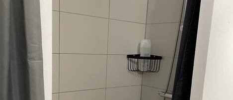 A small, tiled shower area with a showerhead, a soap dispenser, and a towel rack.