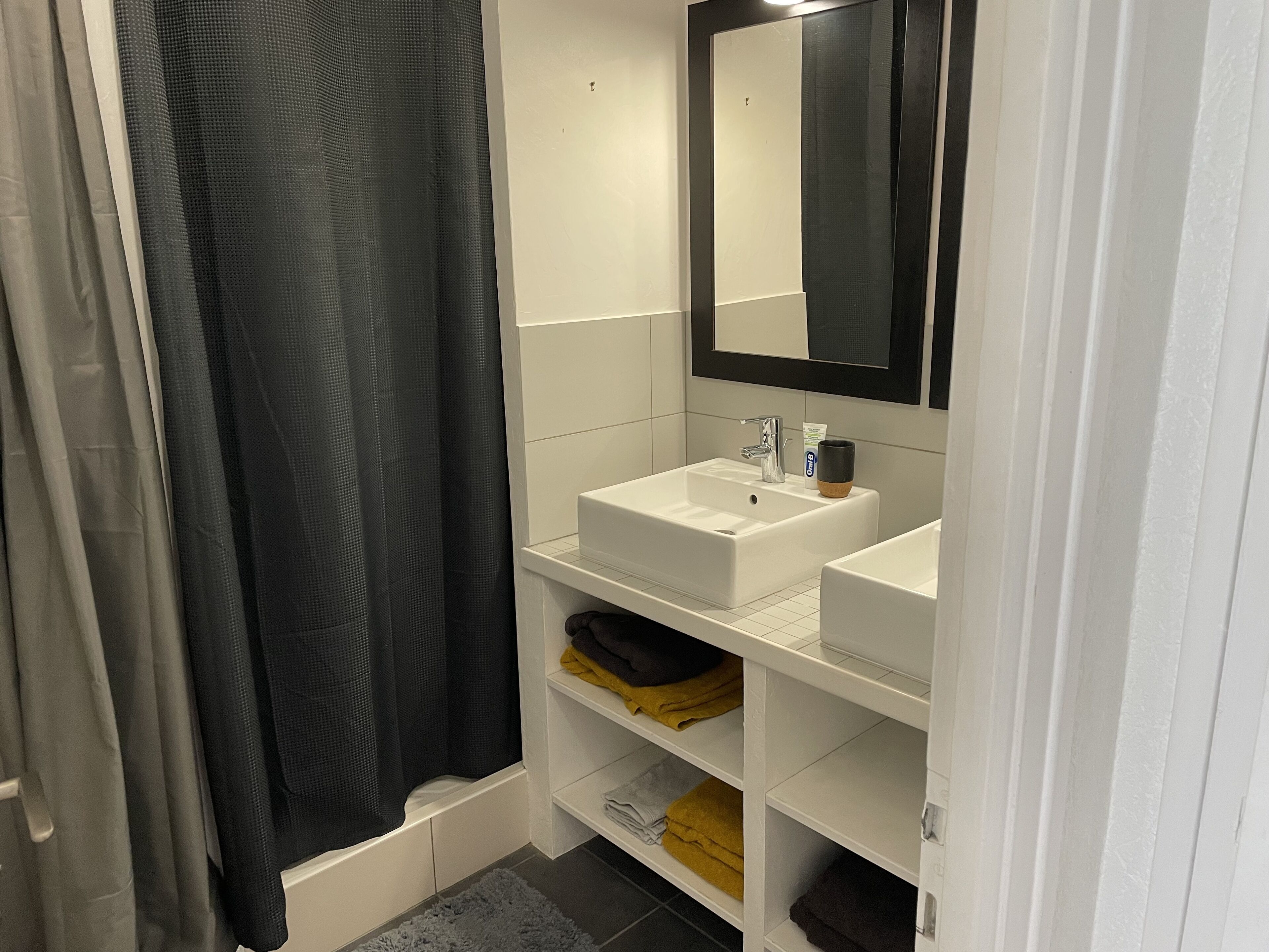 Un baño con lavamanos blanco, espejo y repisas con toallas.