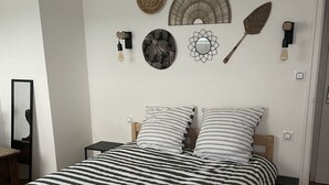 Une chambre avec une couvre-lit à rayures, une décoration murale ronde en fibres tressées, un élément décoratif circulaire fixé au mur et un éventail en bois.