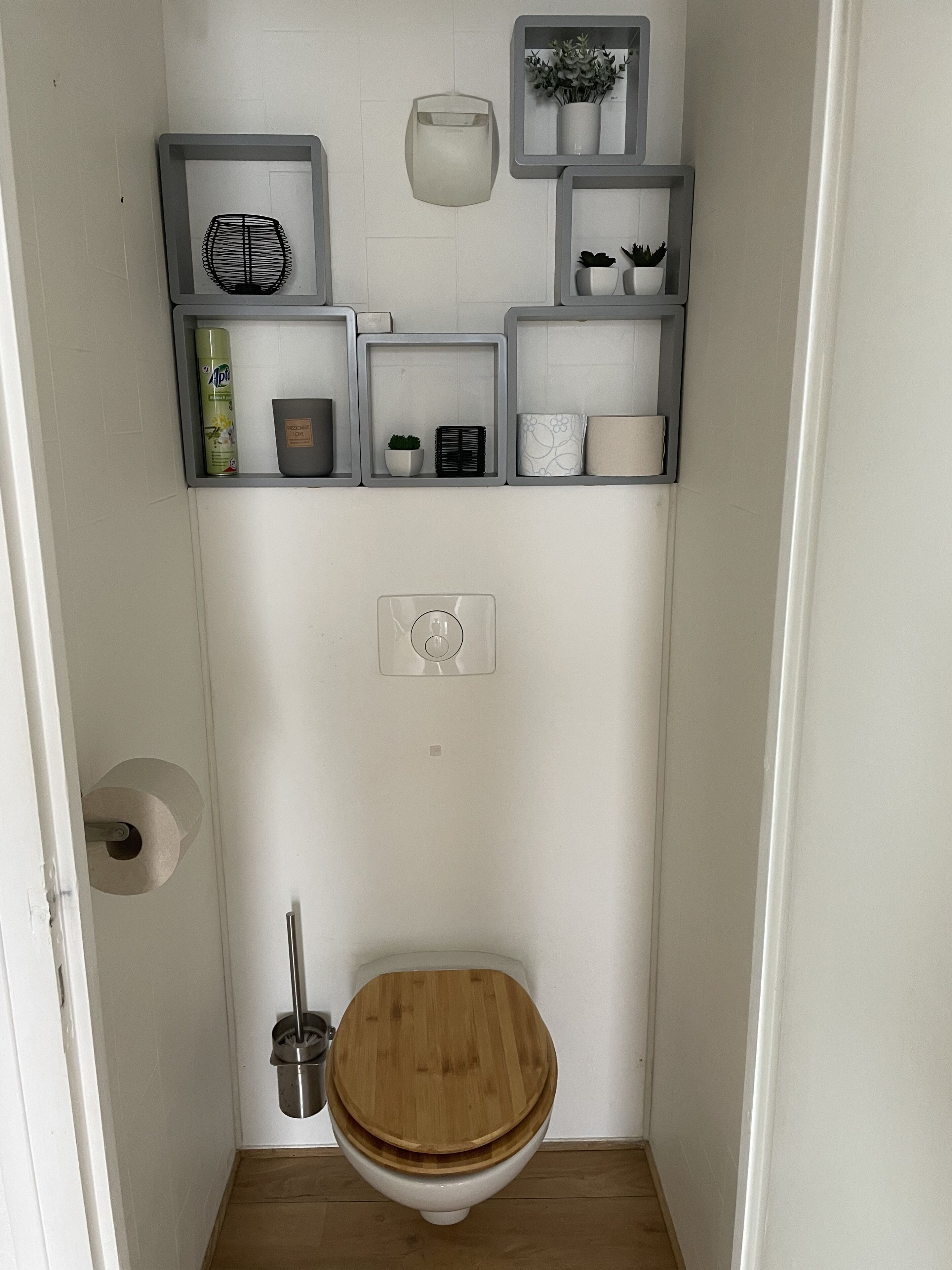 Une petite salle de bain avec des toilettes en bois, une étagère contenant des articles de toilette et un porte-rouleau de papier toilette.