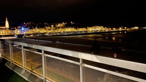Une vue nocturne d’une zone riveraine, avec des bâtiments illuminés et une tour imposante.