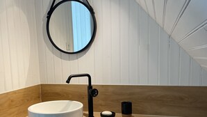 Une salle de bain moderne avec un miroir rond, un lavabo blanc et un plan de toilette en bois.