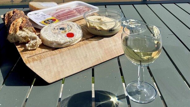 Une table avec des plats et un verre de vin blanc sur un balcon donnant sur une plage.