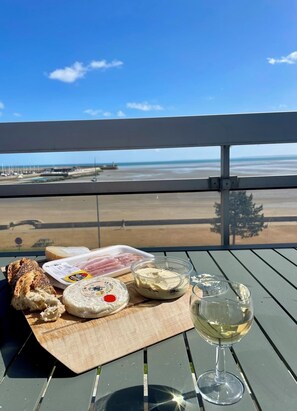 A table with food items and a glass of white wine on a balcony overlooking a beach. - La Terrasse de Binic (Binic-Étables-sur-Mer)