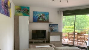 En stue med fjernsyn, sofa, billeder og en balkon med udendørs møbler.