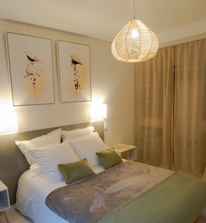 Un lit bien fait, agrĂ©mentĂ© dâoreillers blancs et verts, un luminaire suspendu et deux Ćuvres dâart accrochĂ©es au mur.