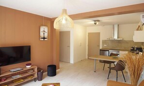 Un salon moderne dotĂ© dâun tĂ©lĂ©viseur Ă Ă©cran plat, dâun coin repas avec une table et des chaises, dâune cuisine Ă©quipĂ©e dâune cuisiniĂšre et dâun lave-vaisselle, et dâun luminaire suspendu.