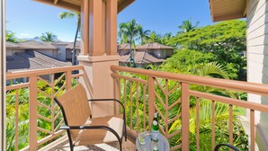 A balcony with a chair and a small table, overlooking a lush garden and neighboring houses. - Vintage tropical townhouse close to pool Colony Villas Bldg 28 (Waikoloa)