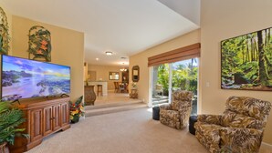 A spacious living room with a large flat-screen TV, a comfortable armchair, and a dining area with a table and chairs. - Vintage tropical townhouse close to pool Colony Villas Bldg 28 (Waikoloa)