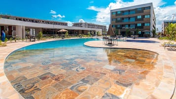 Piscina com design de azulejos único, cercada por área de estar externa e um edifício moderno ao fundo.