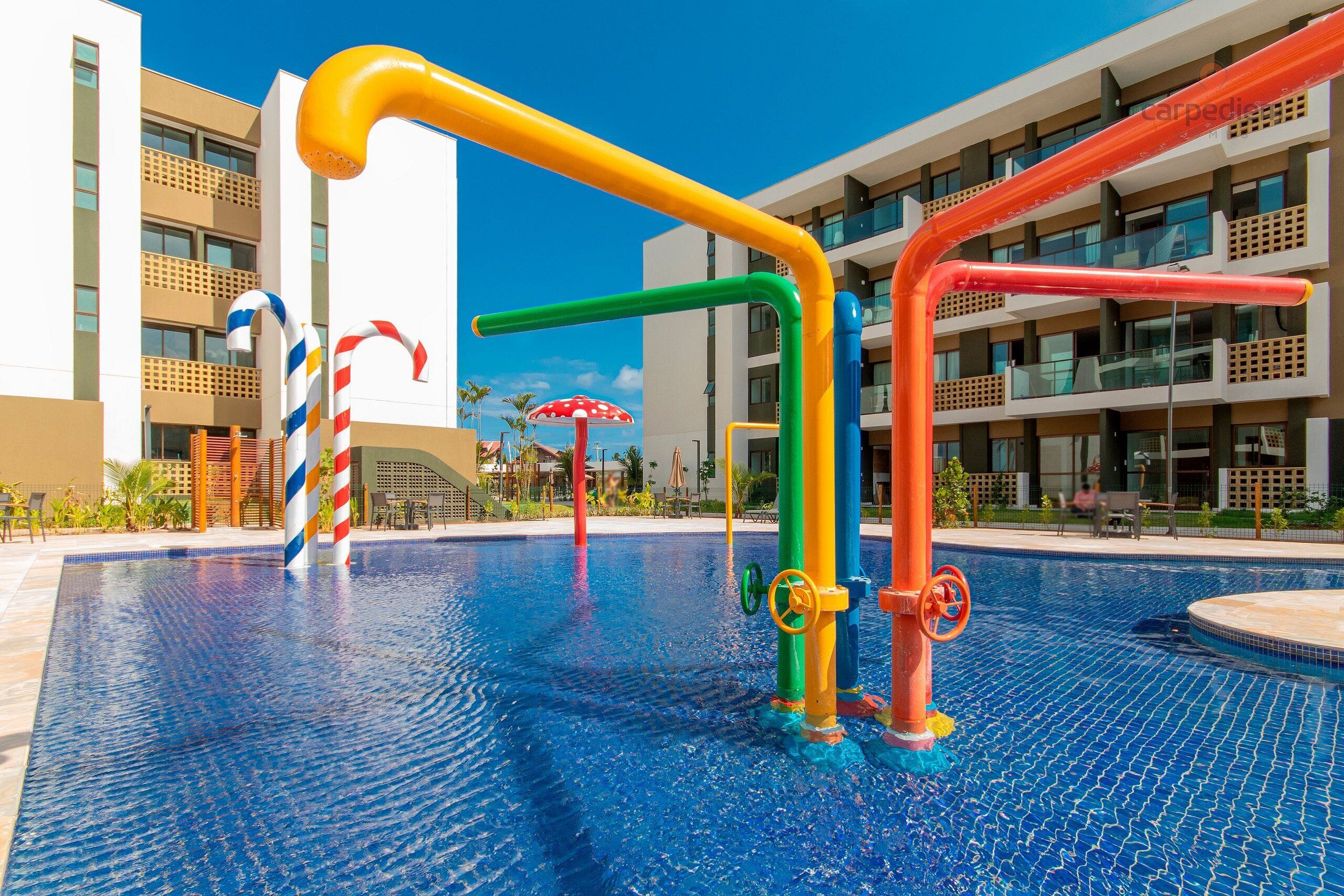A swimming pool with colorful play structures and a modern building in the background.