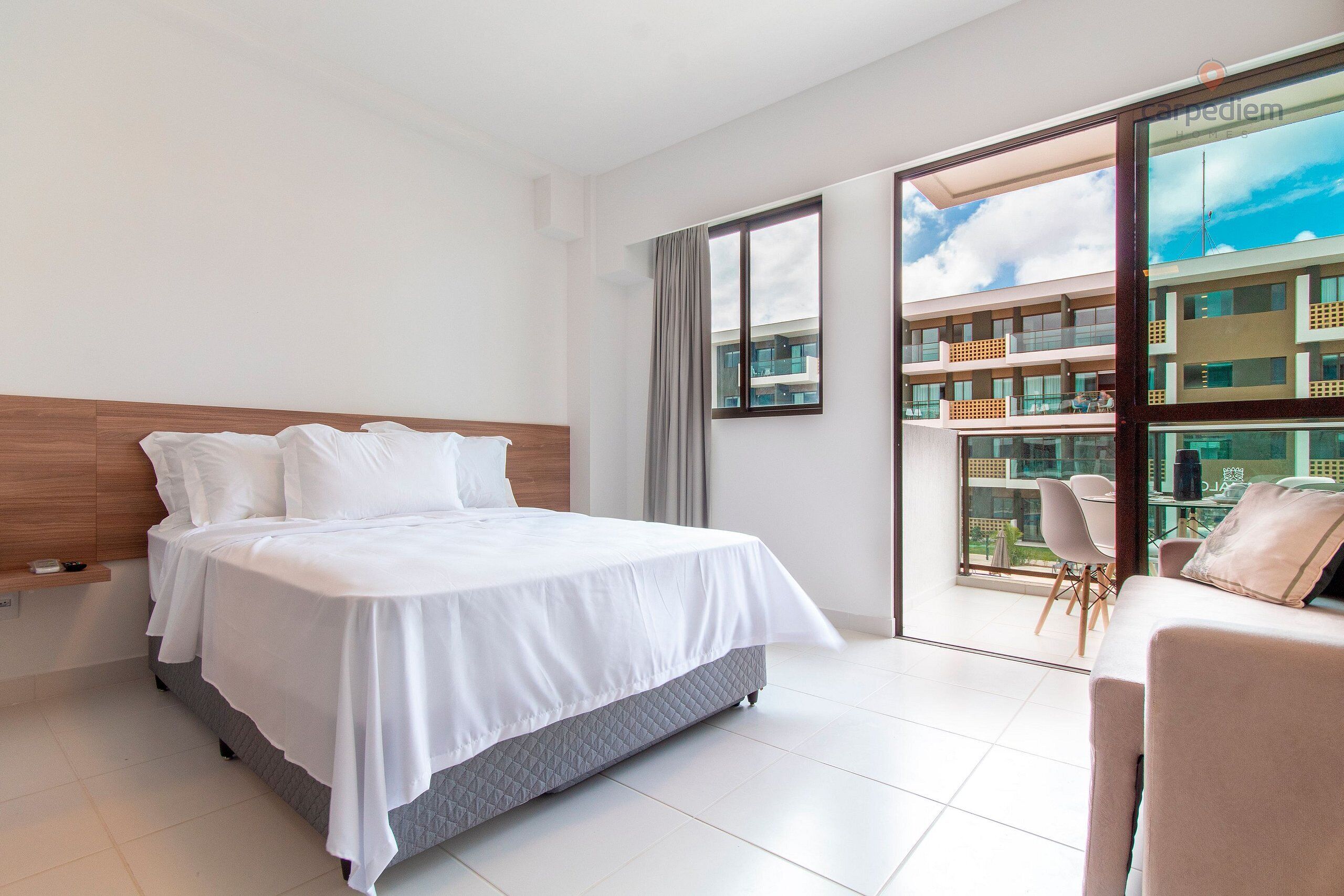 A modern hotel room with a large bed, a sofa, and a balcony with a view of the city.
