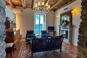 Un salon chaleureux avec un lustre, une cheminée et une vue sur l’extérieur.