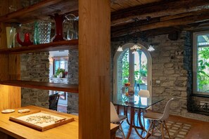 Un intérieur rustique avec des murs en pierre, des poutres en bois, une table en verre et un lustre.