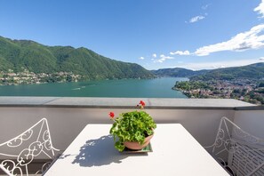 Varanda com mesa e cadeiras, vista para um lago e montanhas.