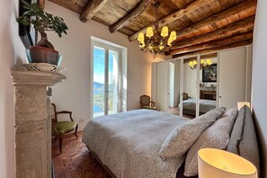 Une chambre à coucher avec un lit, un lustre, un miroir et une vue par la fenêtre.