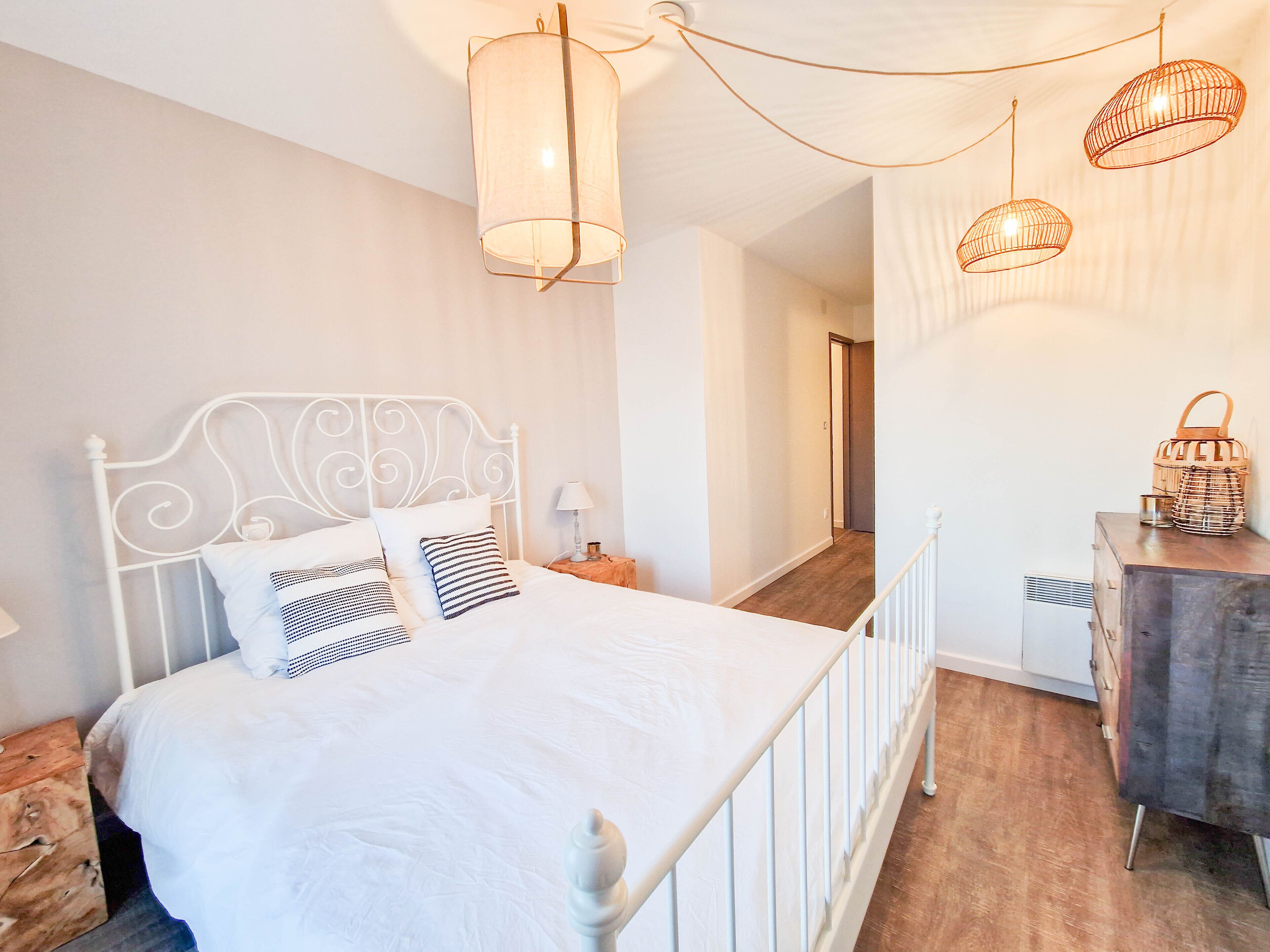 Ein Schlafzimmer mit weißem Metallbettgestell, einem Holzkleiderschrank und einer Pendelleuchte.