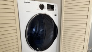 A Samsung front-loading washer and dryer stacked in a cabinet with a sliding door.