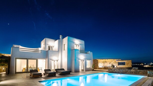 Eine moderne Villa mit Swimmingpool, Sitzgelegenheit im Freien und einer Steinmauer.