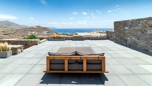 Eine Dachterrasse mit einer Holzbank, Steinmauern und Blick auf das Meer und die Ferne.