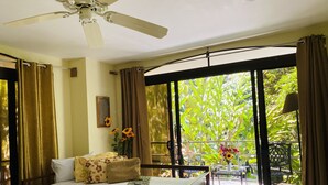 Un dormitorio con cama, ventilador de techo, ventana con cortinas y vista a zonas verdes.
