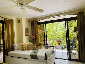 Relax in this stylish room with a large bed, ceiling fan, and balcony offering a view of lush greenery.