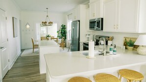 A modern kitchen with white cabinetry, a central island, and a dining area with a chandelier. - Family Friendly House - Resort Style Amenities & Baby Gear (Beaufort)