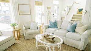 A bright living room with a white sofa, a glass coffee table, and a staircase. - Family Friendly House - Resort Style Amenities & Baby Gear (Beaufort)