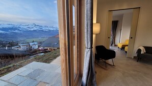 A room with a large window overlooking a snowy mountain landscape. There is a black chair and a sofa in the room.