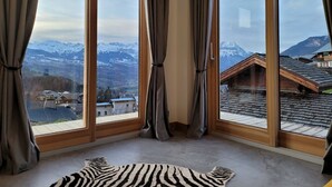 A room with large windows offering a view of snow-capped mountains and a village below.