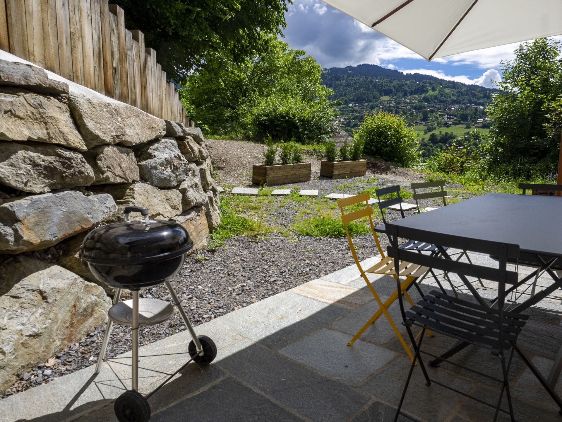 Un patio al aire libre con pared de piedra, una parrilla, una mesa y sillas.
