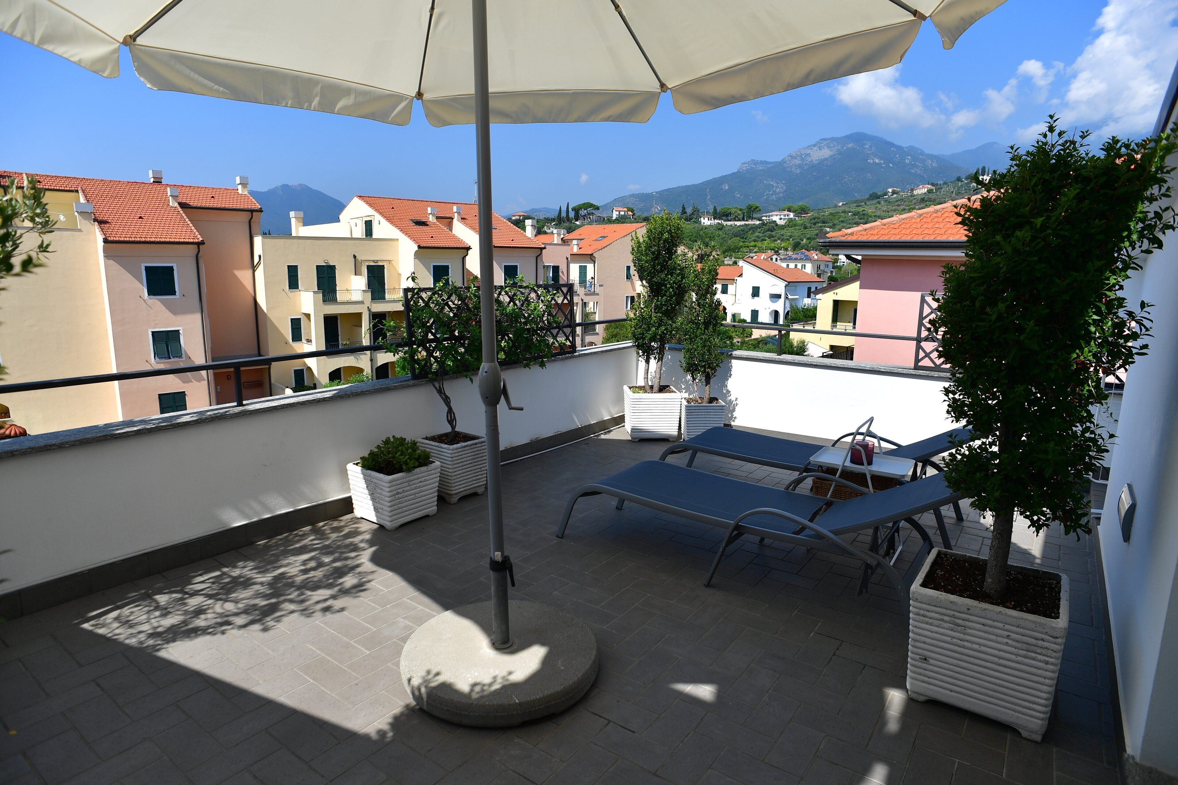 Una terrazza sul tetto con un ombrellone, poltrone da relax, piante in vaso e vista sugli edifici e sulle montagne circostanti.