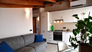 Une cuisine moderne avec des meubles blancs, un canapé gris agrémenté de coussins bleus et un coin repas avec une table en verre.