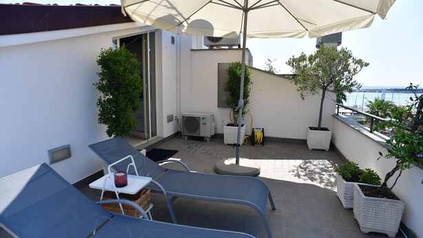 Une terrasse sur le toit avec deux chaises longues, une table avec une bougie, des plantes en pot et une vue sur la mer.