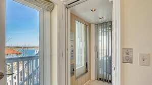 Un couloir avec une porte d’ascenseur en verre, une vue sur la mer et un balcon doté d’une balustrade.