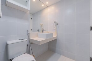 Une salle de bain moderne avec des toilettes blanches, un lavabo surmonté d’un miroir et un espace douche.