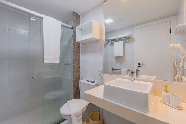 Un baño moderno con cabina de ducha de vidrio, inodoro, lavamanos con espejo y secador de pelo en la encimera.