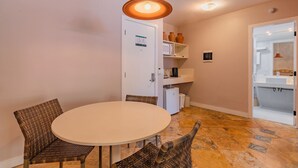 A compact living space with a round dining table, two wicker chairs, a white door with a map, a microwave, and a small refrigerator. - Apart no Beach Park Suítes por Carpediem (Aquiraz)