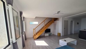 Een moderne woonkamer met een houten trap, een flatscreen televisie, een blauwe bank en een plafondventilator.