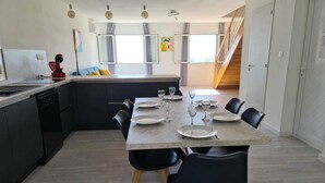 Een moderne keuken met een eethoek, met een groot kookeiland, zwarte stoelen en een houten trap.