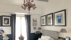 A bedroom with a large bed, a chandelier, framed artwork on the walls, and a window with curtains. - 500 m from Roland Garros stadium, apartment with terrace (6-8 people) (Boulogne-Billancourt)