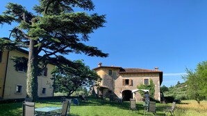 A traditional building with a tiled roof and stone walls, surrounded by a well-maintained lawn and outdoor seating area with metal chairs and tables. - Cervano Ecli: apartment for 5 with original fireplaces from 1886 (Lombardia)