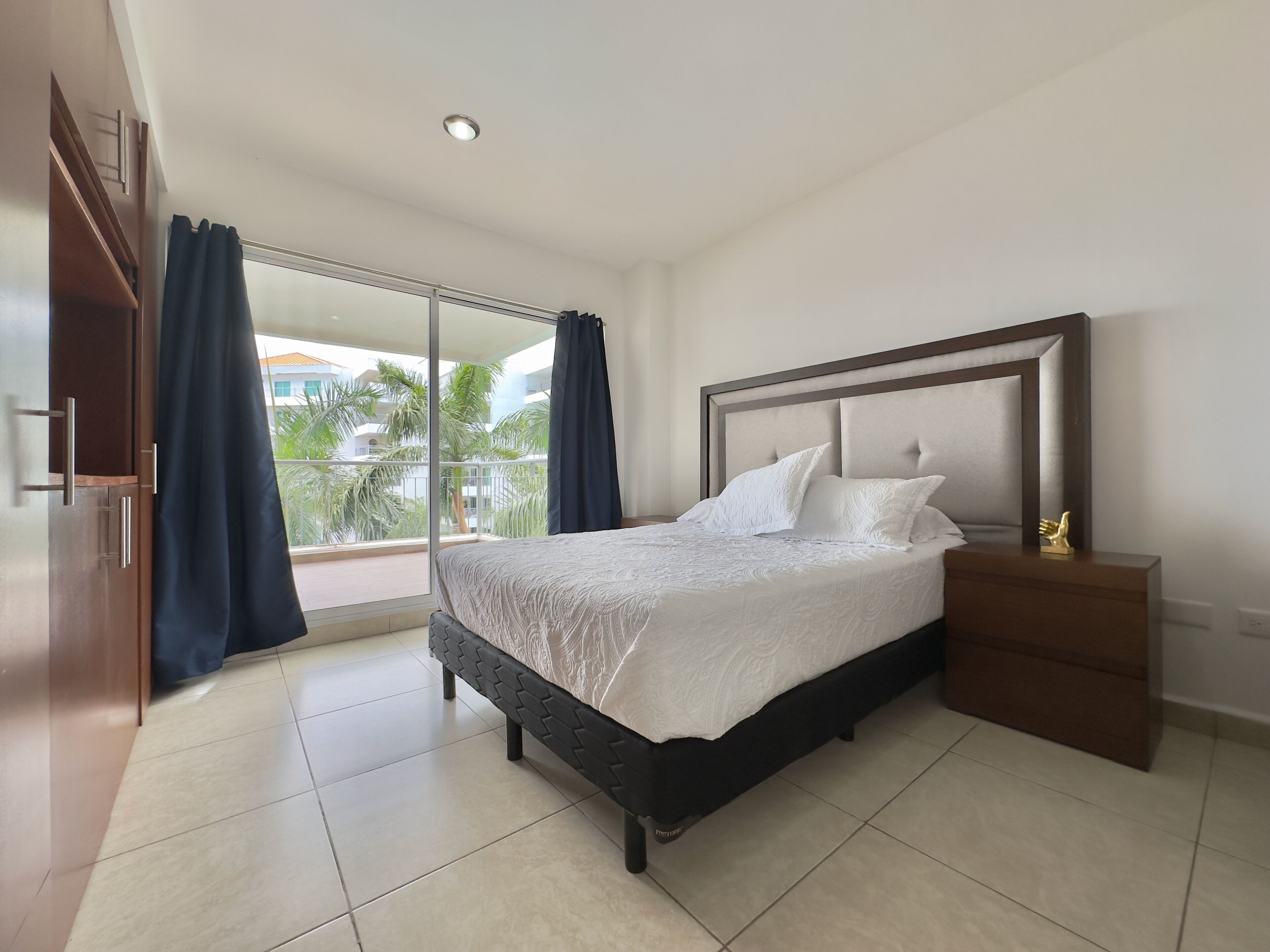 A bedroom with a bed, a nightstand, a wardrobe, and a view of the outside.