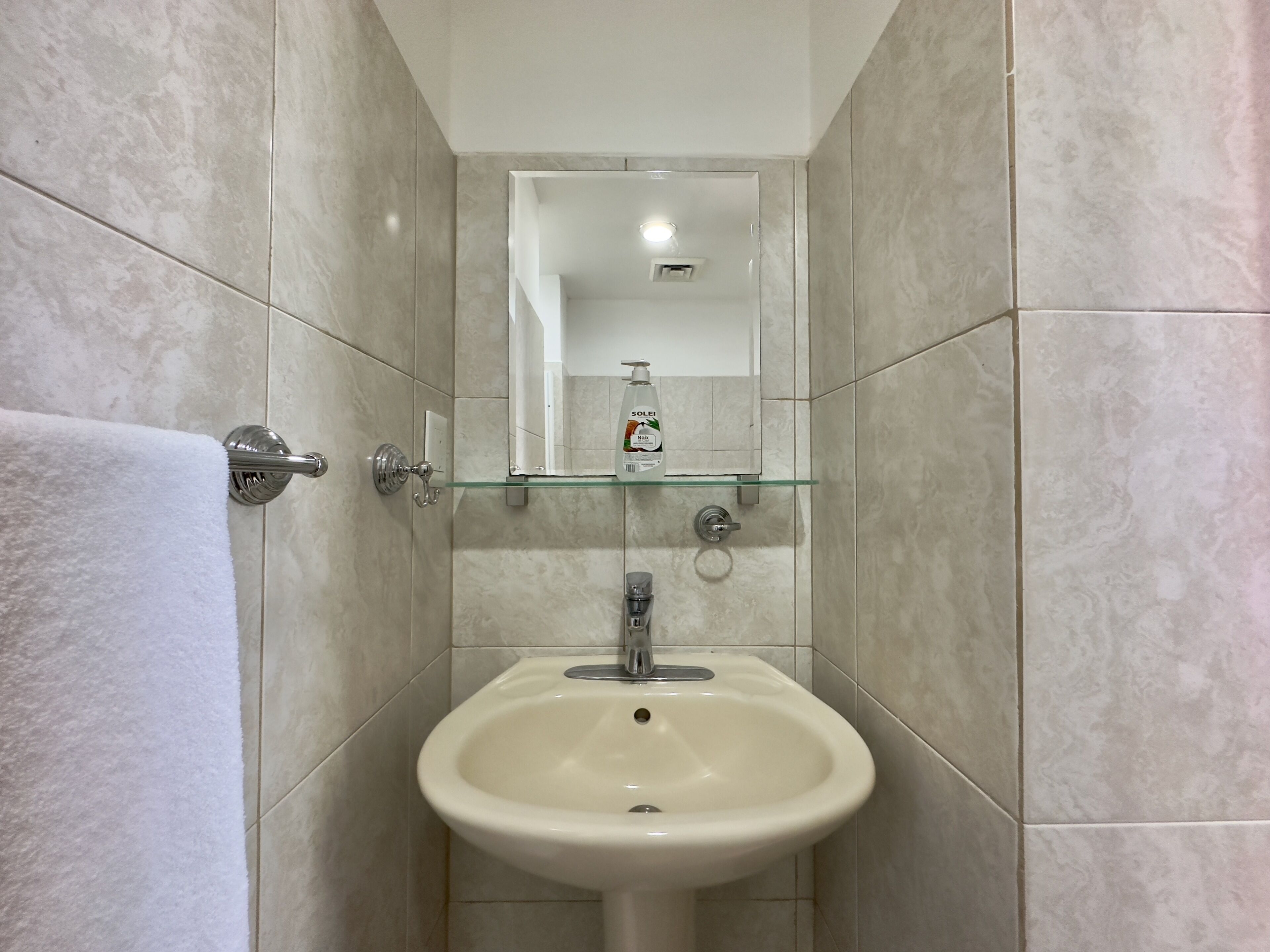 Een badkamer met een wit wastafel, een glazen plank erboven en een handdoek aan een metalen handdoekrek.