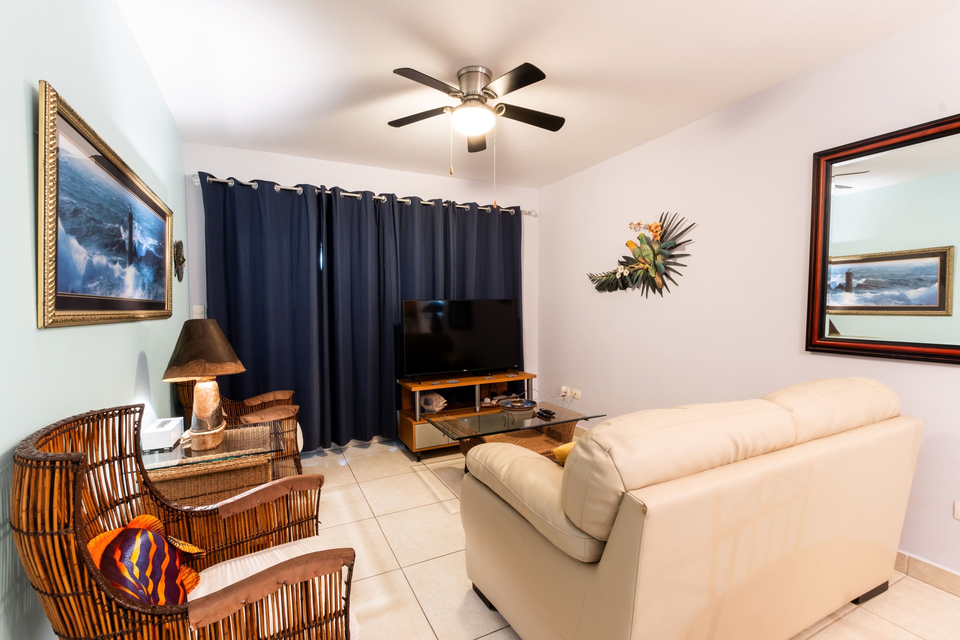 A living room with a sofa, a television, a ceiling fan, and a wall-mounted TV.