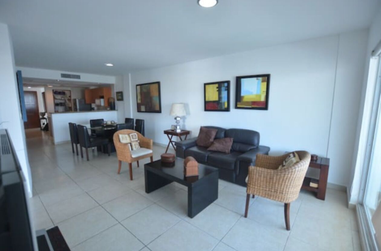 A modern living room with a sofa, two armchairs, a coffee table, and a dining area with chairs and a table.