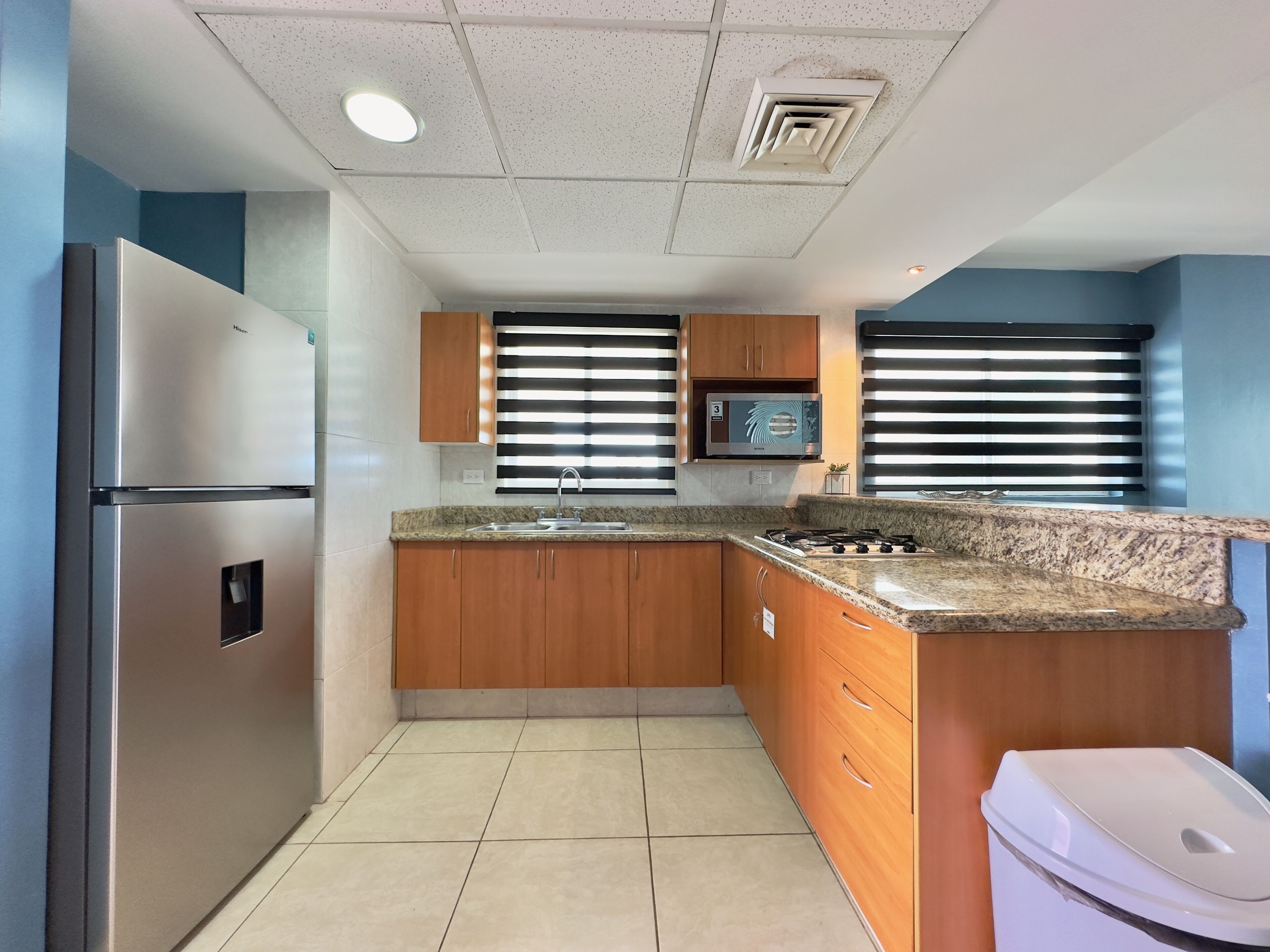 Una cocina moderna con armarios de madera, un refrigerador de acero inoxidable, un microondas y una estufa a gas.